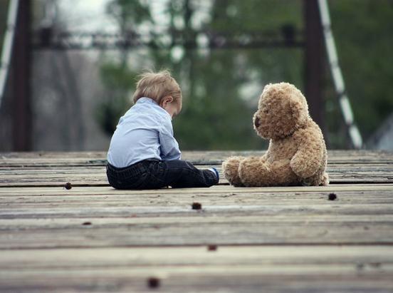 ein kleines Kind sitzt traurig mit einem Teddy auf einem Weg