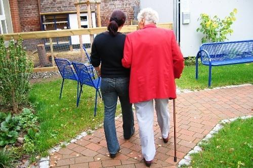 eine Person hilft einer Frau mit Krücke beim Laufen